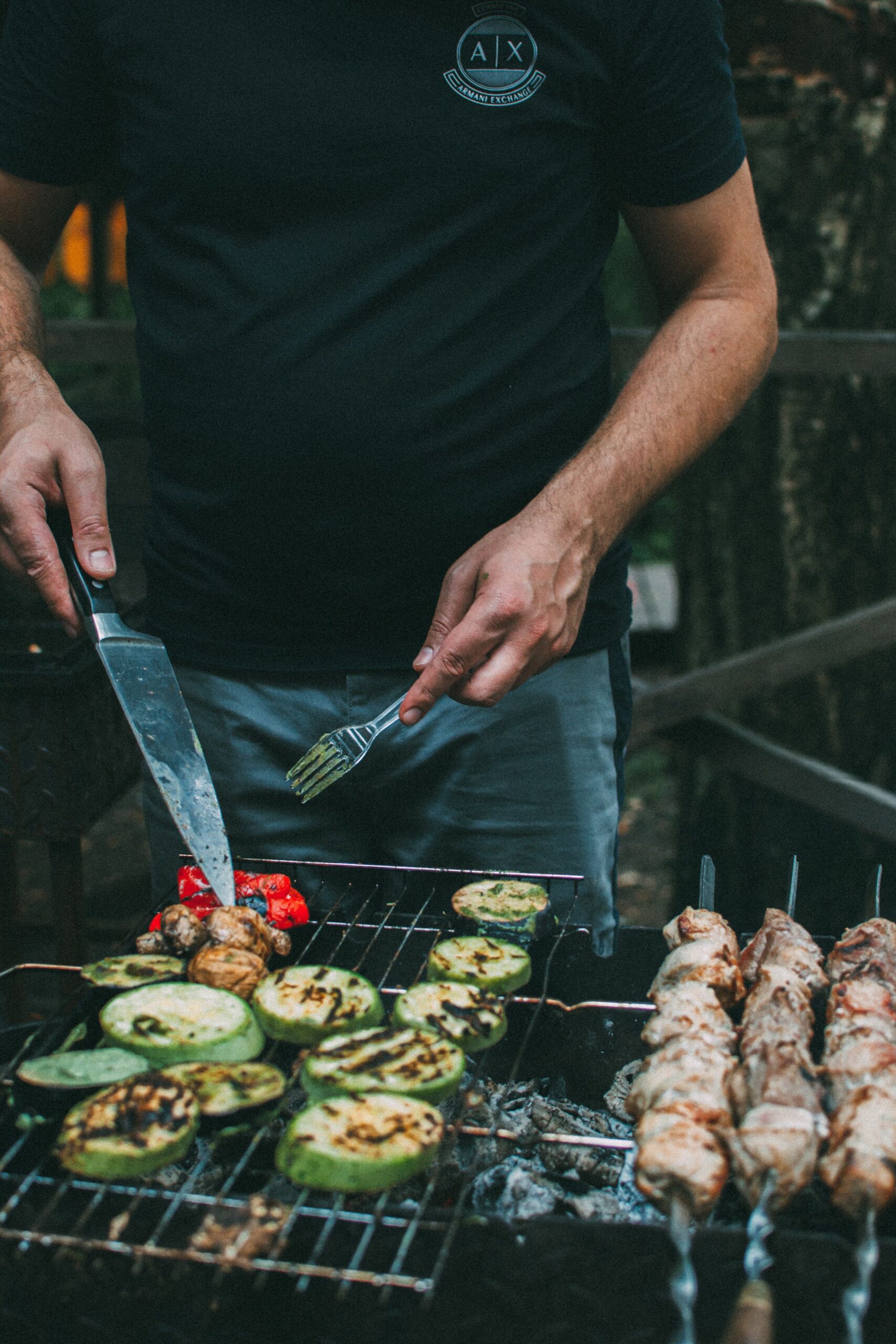 A man grilling vegetables and meat skewers on an outdoor barbecue.